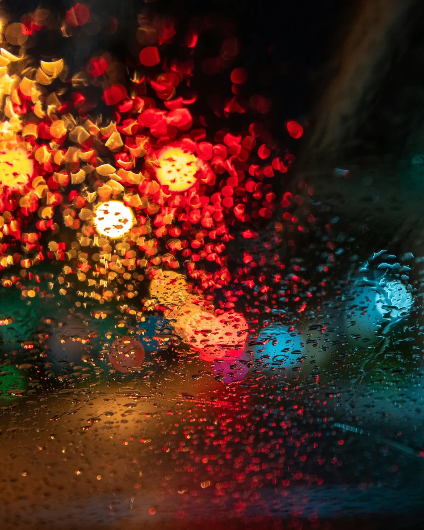 Luces rojas, amarillas y azules desenfocadas a través de un cristal con gotas de lluvia.